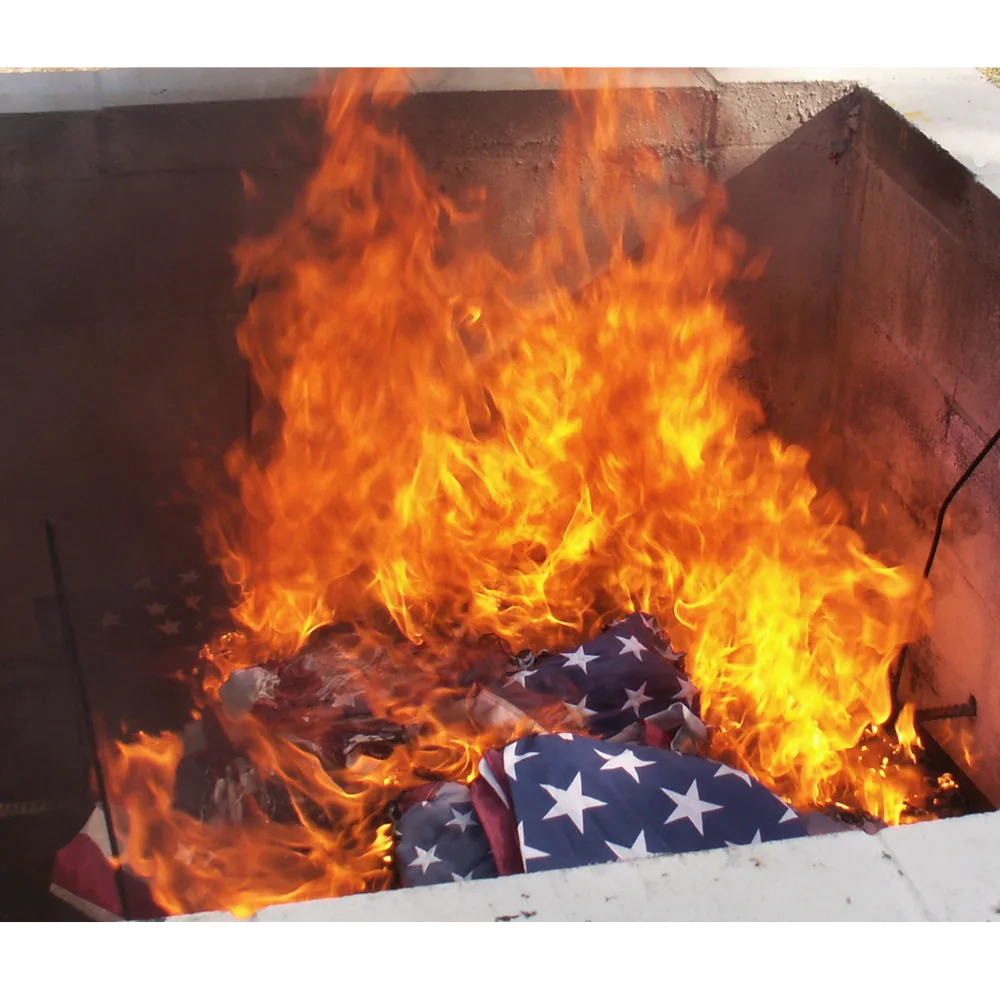 Flag retirement ceremony with several flags burning in a pit